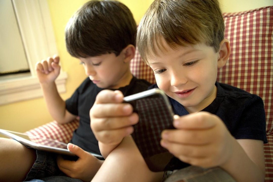 Dos niños jugando con dispositivos electrónicos. 