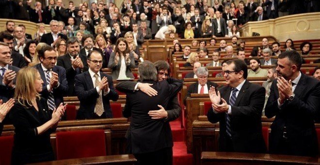 Artur Mas (de espaldas) abraza a Carles Puigdemont, poco antes de comenzar el pleno de investidura en el Parlament.