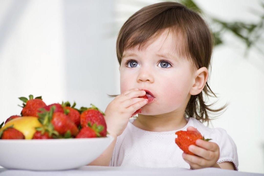 Una niña pequeña comiendo frutas. 