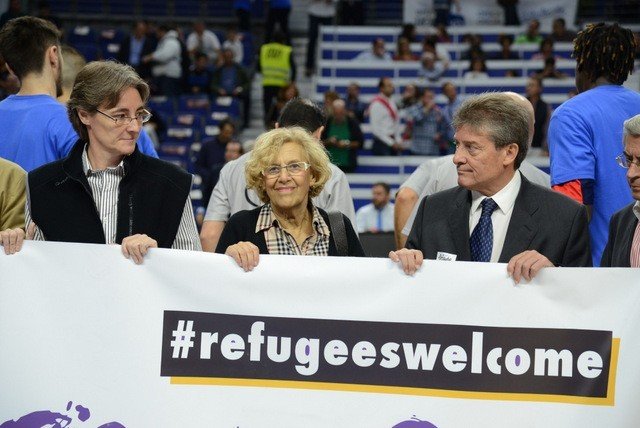Manuela Carmena sostiene un cartel de bienvenida a los refugiados.