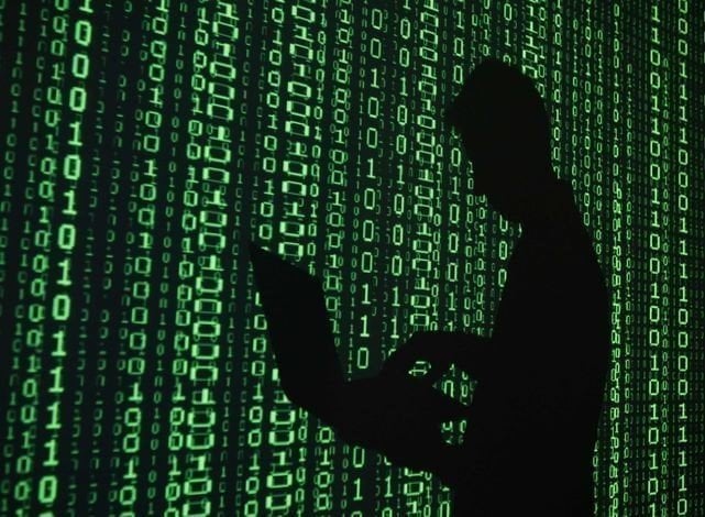 Imagen de un hacker con un ordenador sobre un fondo con el código binario