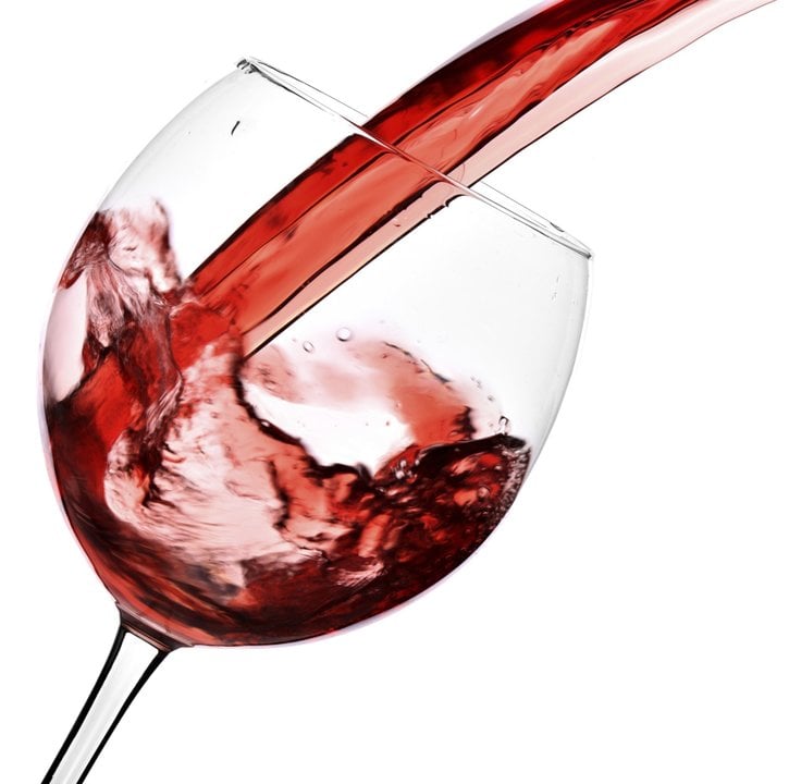 Red wine pour into glass isolated over white background
