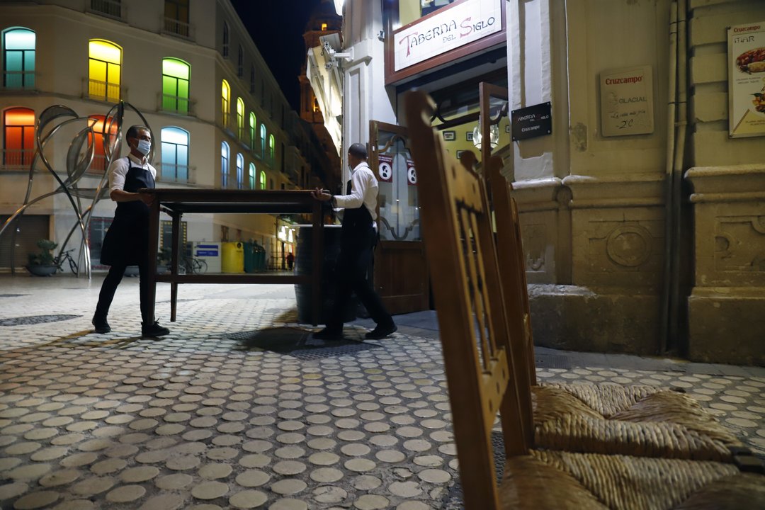 MLG 27-10-2020.-Dos camareros se afanan en recogen la terraza del bar ubicado en el centro de la capital, ha consecuencia del toque de queda impuesto por el Gobierno para poder frenar el contagio de Covid-19.-ÁLEX ZEA.