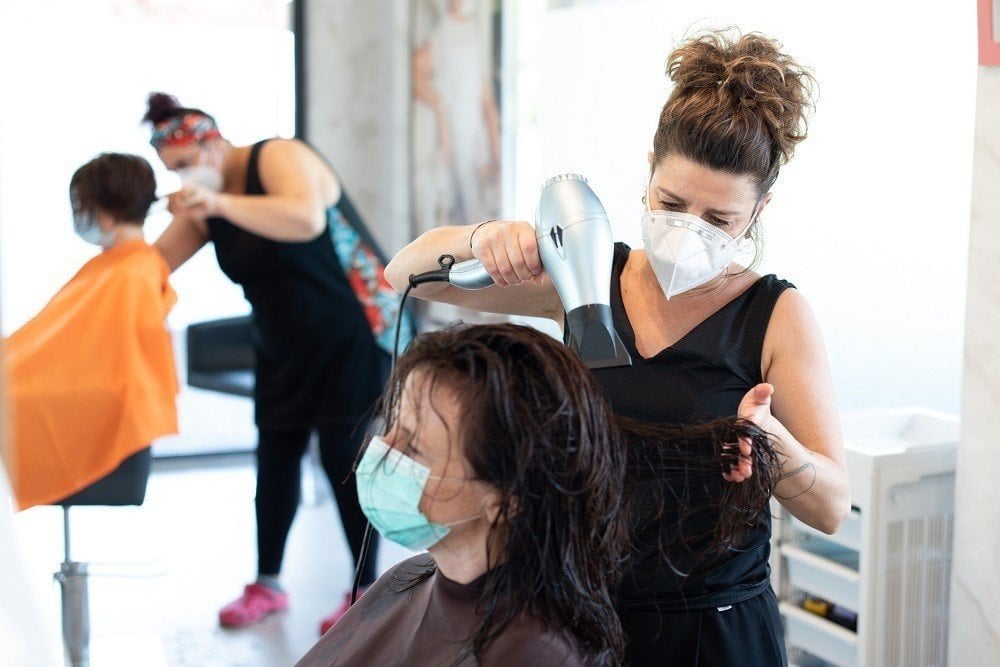 Una peluquera peina a una clienta ambas con mascarillas