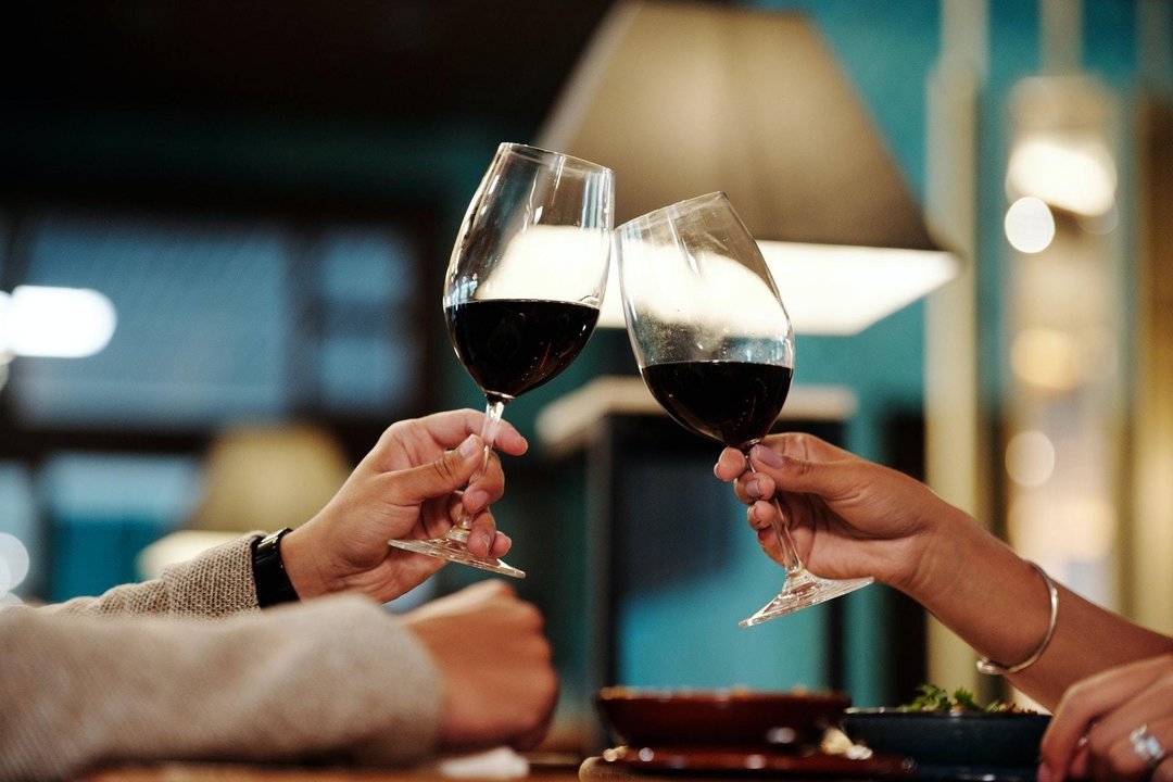 Dos personas brindan con sendas copas de vino tinto.