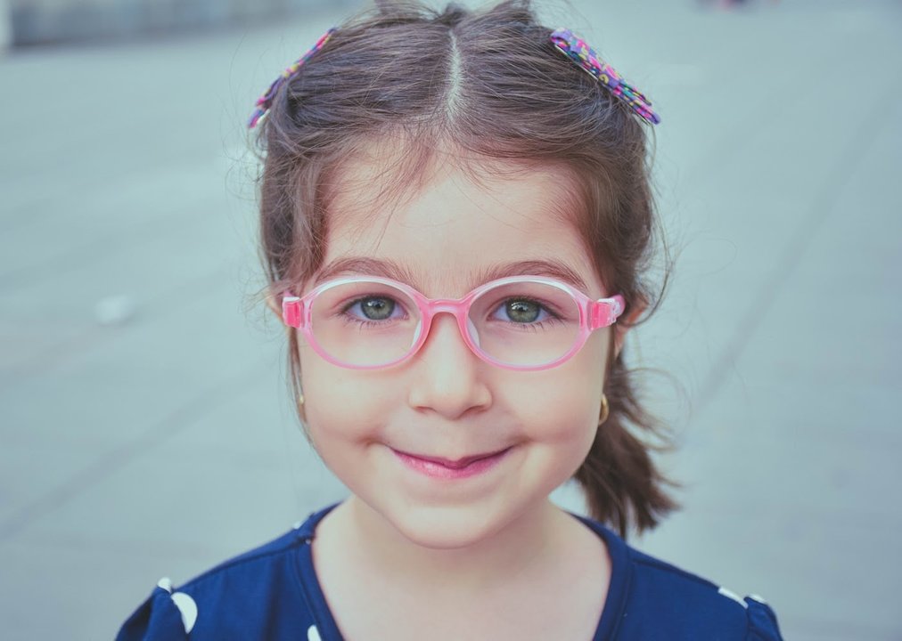 Una niña con gafas sonríe a cámara.