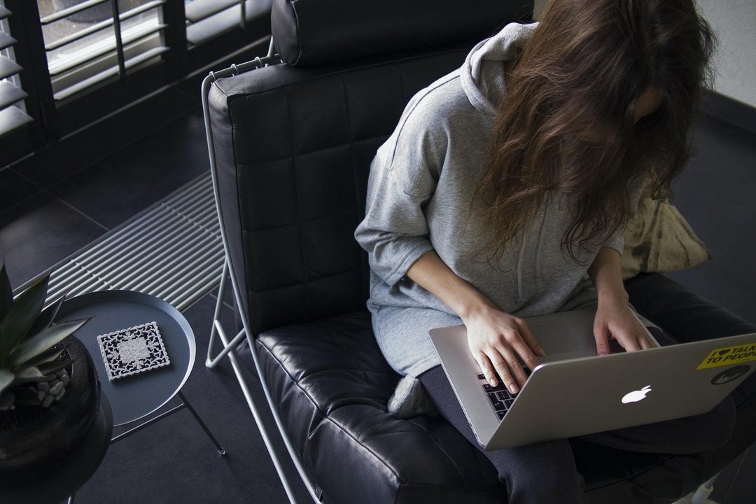 Una mujer sentada con un portátil en las piernas.
