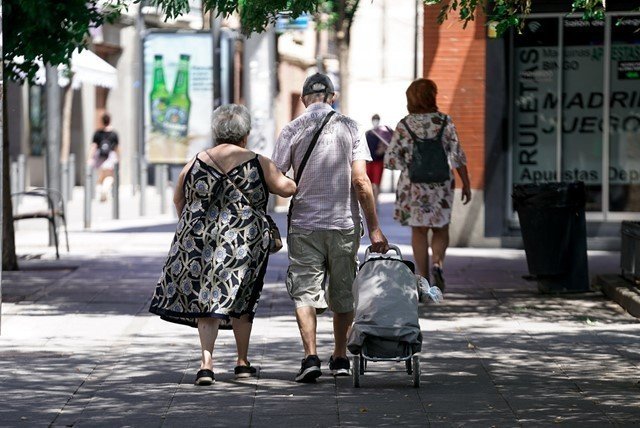 Una pareja de ancianos camina por la calle con un carro de compra en Madrid.
