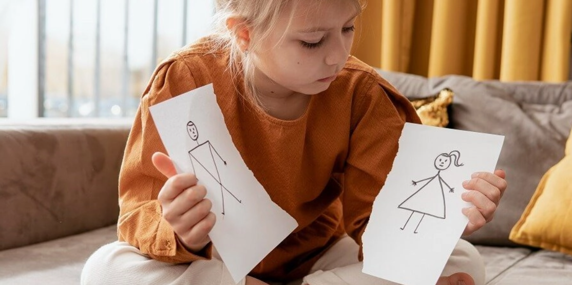 Una niña con el dibujo de un padre y una madre cortado en dos.