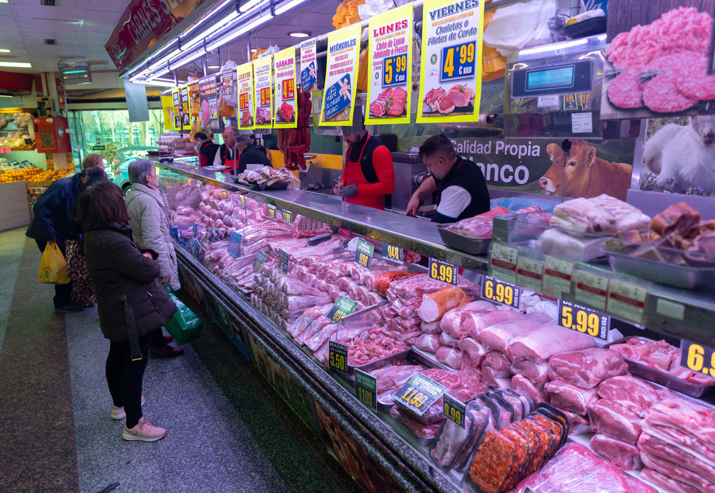 Varias personas compran en una carnicería en un mercado.
