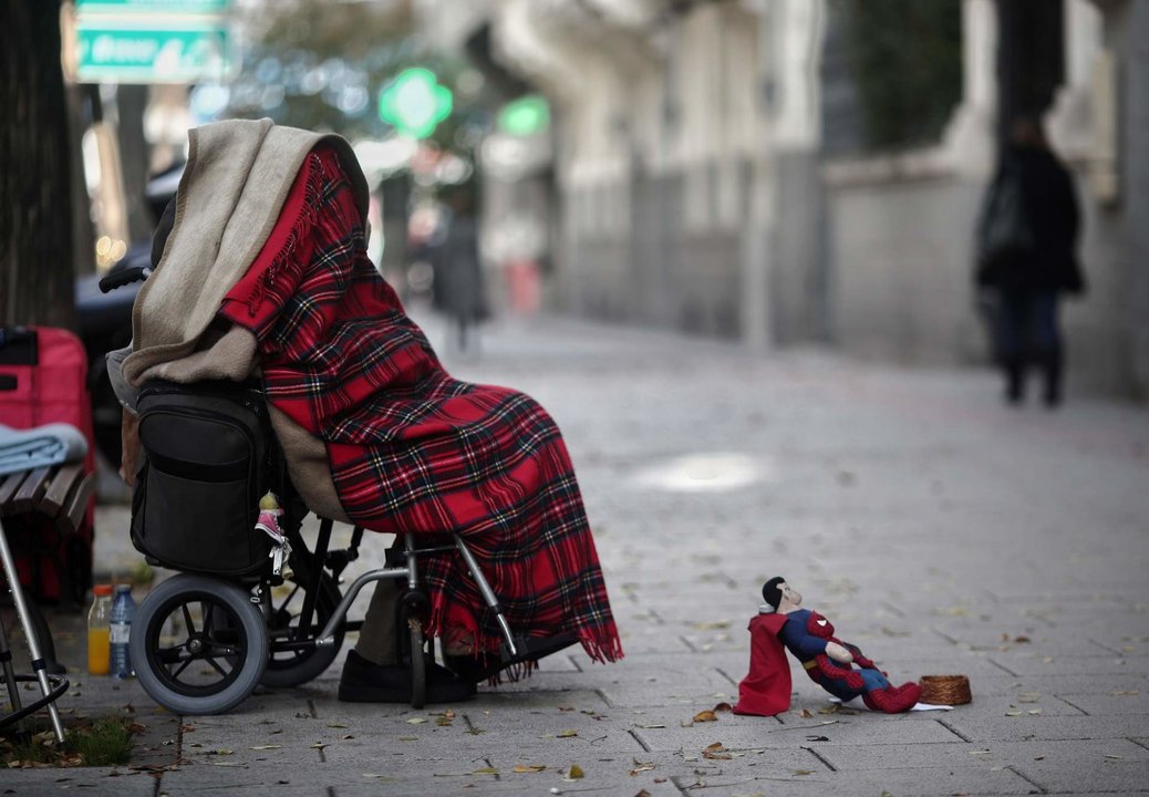 Imagen de archivo de una persona en silla de ruedas y tapada con una manta pidiendo dinero en la calle.