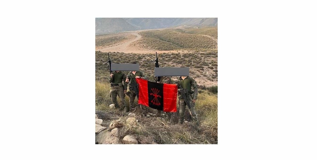 Cuatro militares en un campo de maniobras con una bandera de Falange.