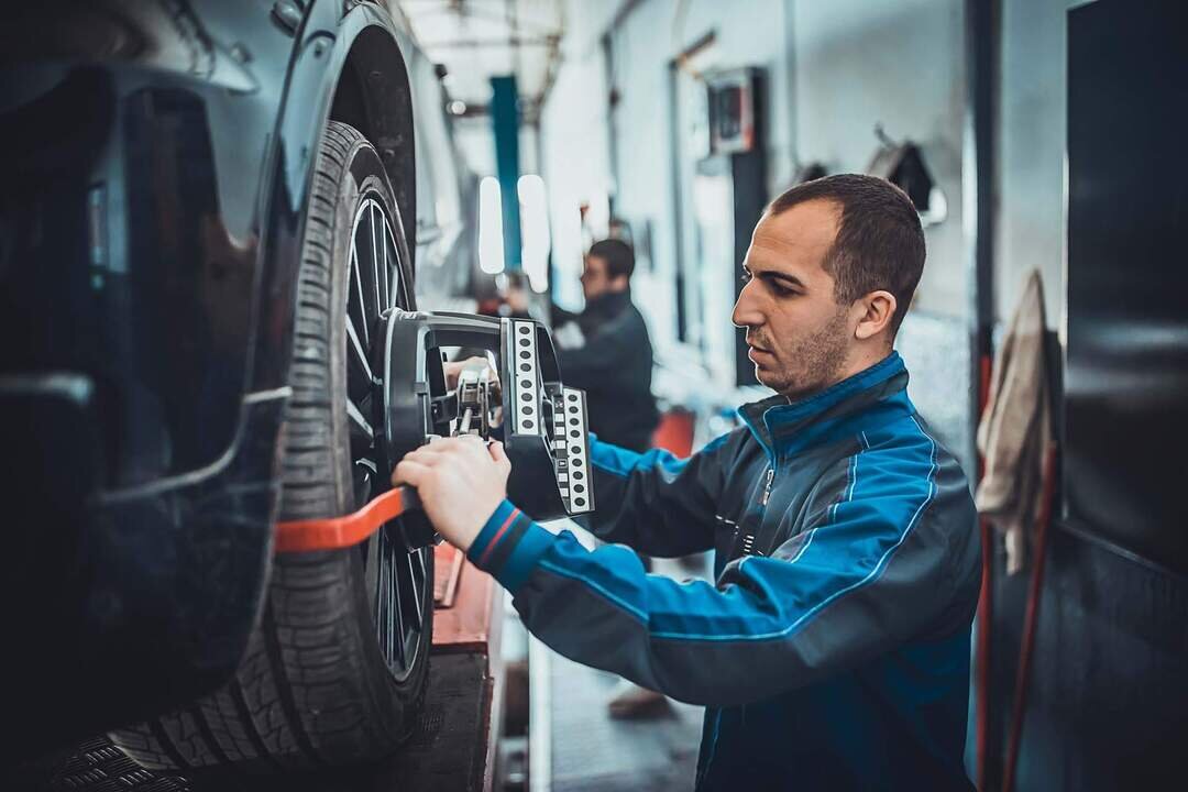 Two young auto mehanic sets the wheel alignment equipment on a car wheel in a repair station.