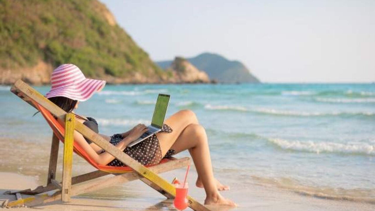 Young attractive woman in dress, sunglasses and hat, working in laptop on the beach