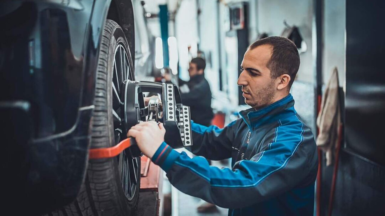 Two young auto mehanic sets the wheel alignment equipment on a car wheel in a repair station.