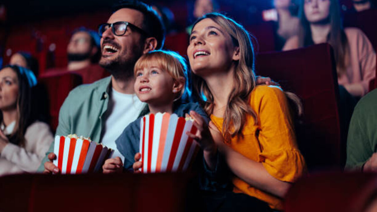 A young joyful couple is with their daughter in the cinema, watching an exciting movie.