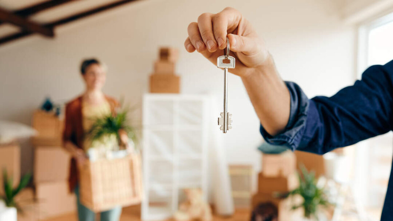 Close-up of a man holding new house key while relocating in a new home with his wife.