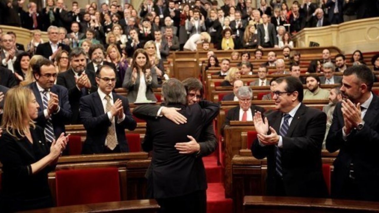 Artur Mas (de espaldas) abraza a Carles Puigdemont, poco antes de comenzar el pleno de investidura en el Parlament.