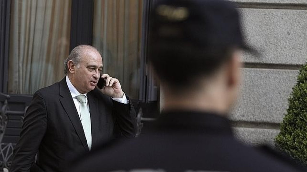 Jorge Fernández Díaz habla por teléfono ante la mirada de un Policía.