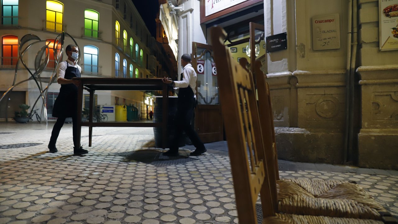 MLG 27-10-2020.-Dos camareros se afanan en recogen la terraza del bar ubicado en el centro de la capital, ha consecuencia del toque de queda impuesto por el Gobierno para poder frenar el contagio de Covid-19.-ÁLEX ZEA.