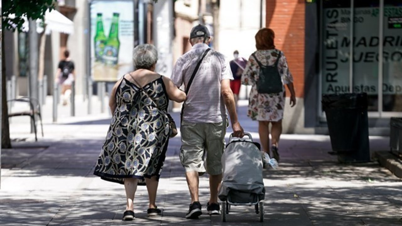 Una pareja de ancianos camina por la calle con un carro de compra en Madrid.
