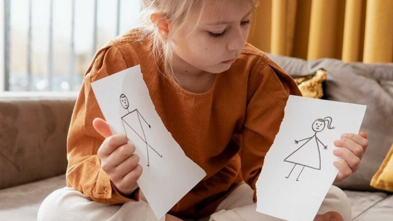Una niña con el dibujo de un padre y una madre cortado en dos.
