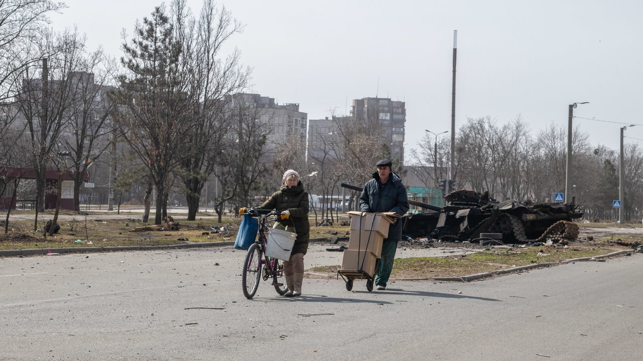A couple wheels Russian humanitarian aid past a destroyed tank in central Mariupol. The battle between Russian / Pro Russian forces and the defencing Ukrainian forces lead by Azov battalion continues in the port city of Mariupol.