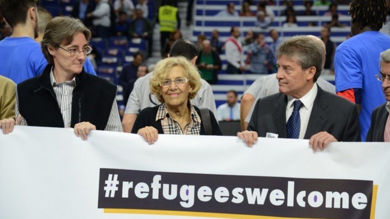 Manuela Carmena sostiene un cartel de bienvenida a los refugiados.