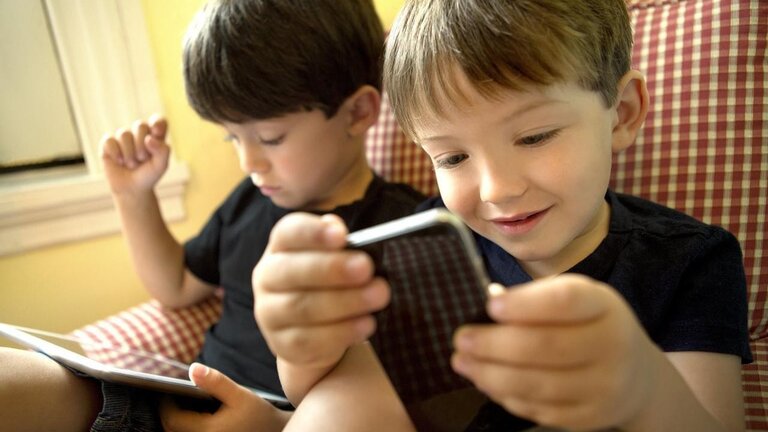 Dos ni&ntilde;os jugando con dispositivos electr&oacute;nicos. 